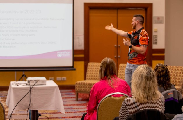 Josh in front of a crowd presenting.