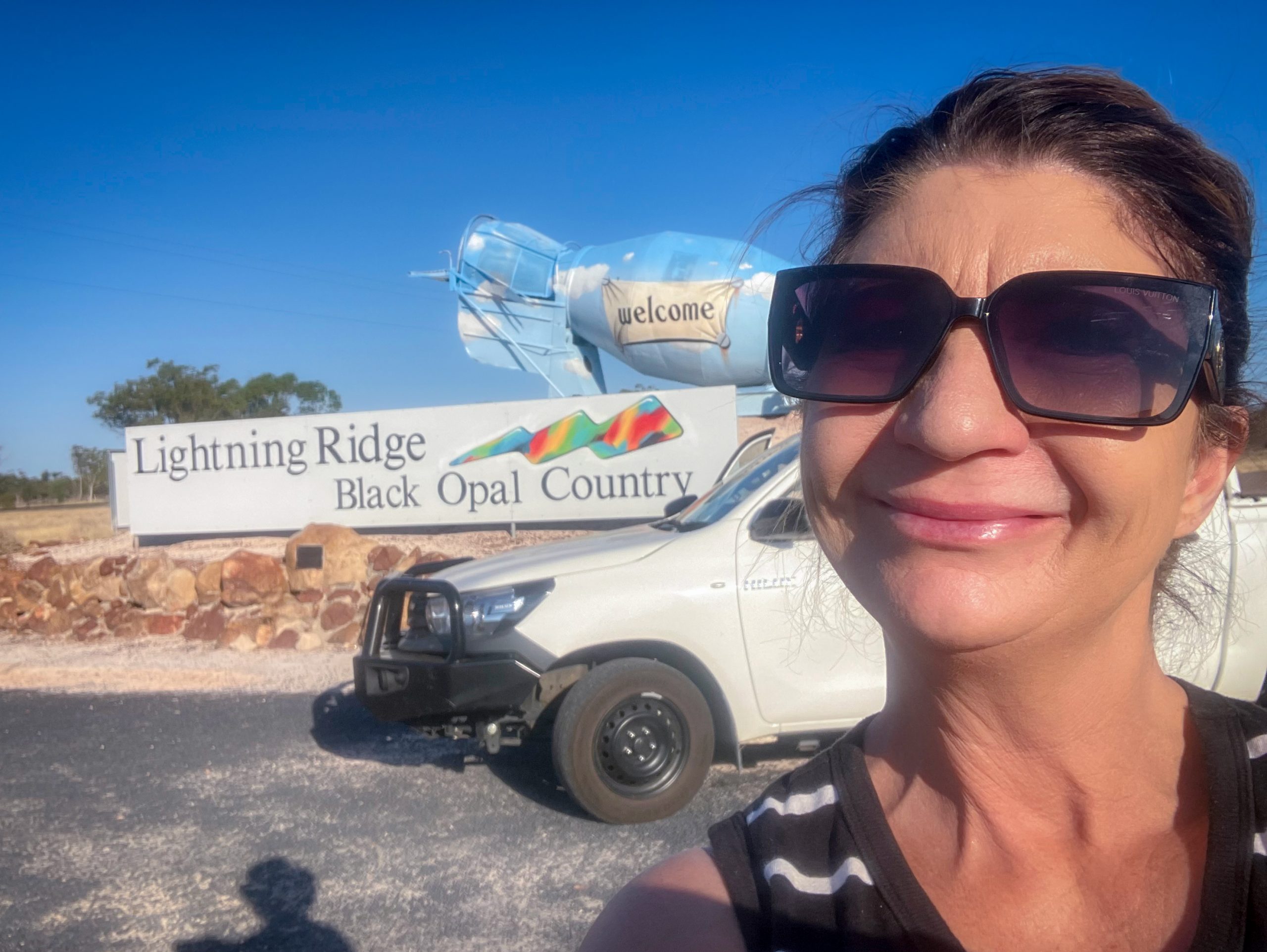 Alana is smiling at the camera in front of the Lightning Ridge sign